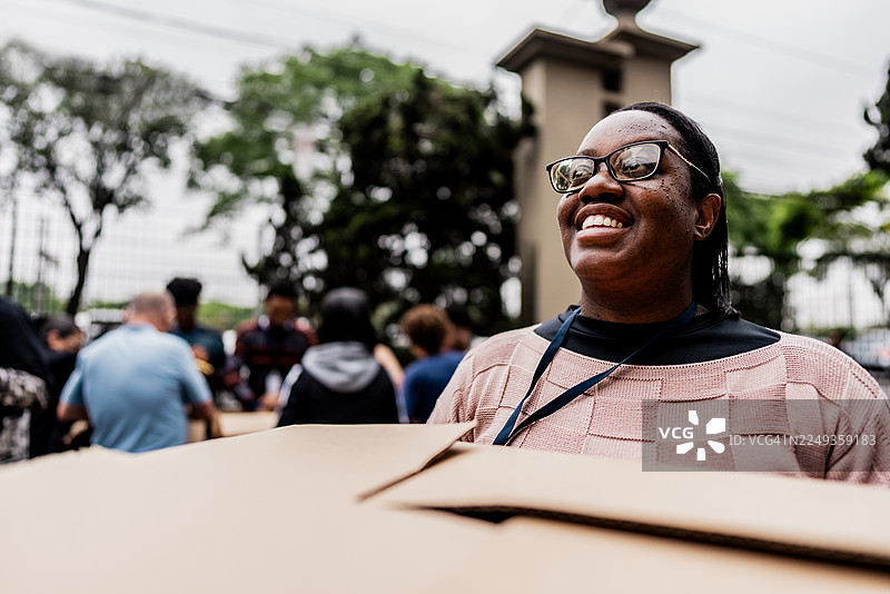 一位女性志愿者在社区活动中，手持纸箱若有所思。图片素材