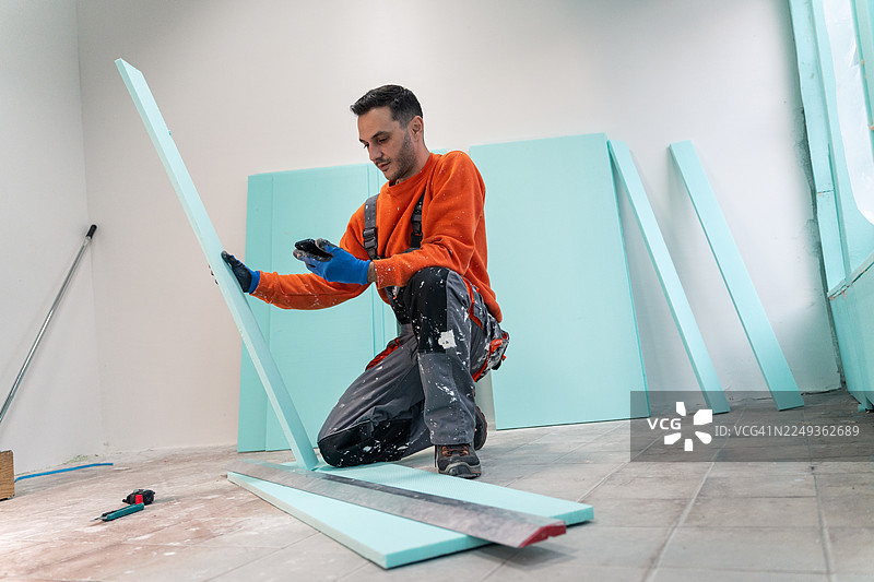 熟练工人一边看手机上的视频教程，一边进行XPS保温材料的施工。图片素材