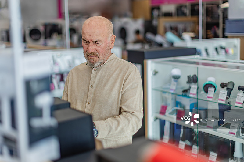 顾客在电子产品商店选购现代科技产品，仔细查看各种商品。图片素材