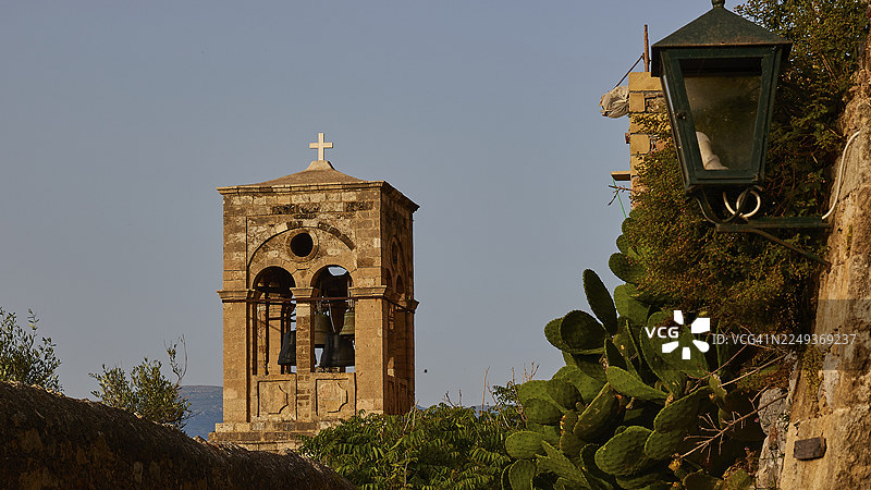 柔和的晨光,锁链圣母教堂,埃尔科梅诺斯·克里斯托斯,带有十字架的钟楼,旁边是蓝天下的古老石墙,周围绿意盎然,莫奈姆瓦夏,马尔瓦西亚,拜占庭小镇,岩石岛,堡垒,拉科尼亚,伯罗奔尼撒,佩图片素材