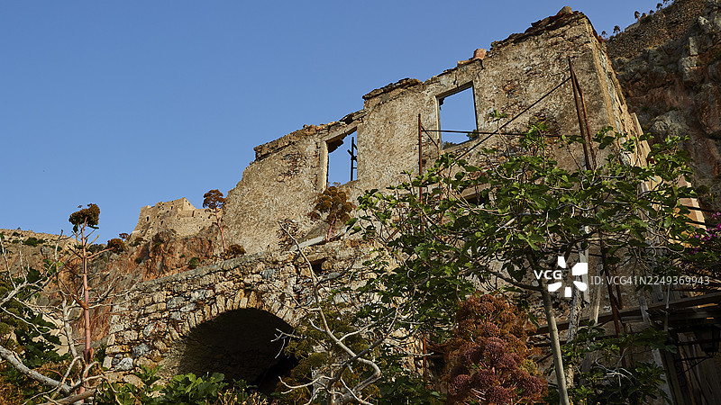 坐落于青翠植被下的斑驳石头建筑，天空晴朗，莫奈姆瓦夏，马尔瓦西亚，拜占庭小镇，岩石岛，堡垒，拉科尼亚，伯罗奔尼撒，半岛，希腊图片素材