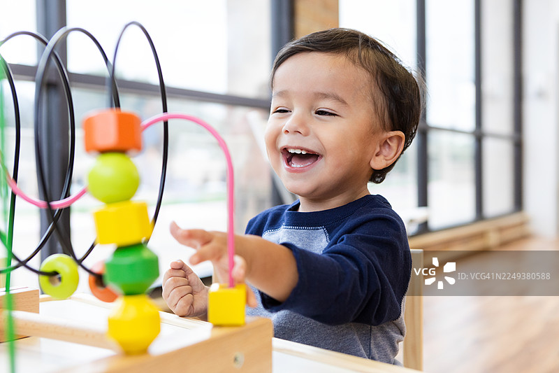 一个快乐的幼儿男孩，在明亮的房间里玩着彩色的珠子迷宫玩具，开心地大笑图片素材