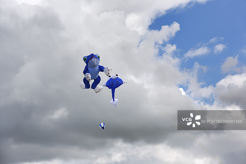 两只风筝在雨云前飞翔，蓝色的青蛙和蝌蚪，在德国北莱茵-威斯特法伦州埃格山脉自然公园和南部条顿堡森林、威悉山地地区的温瑟贝克风筝节上图片素材