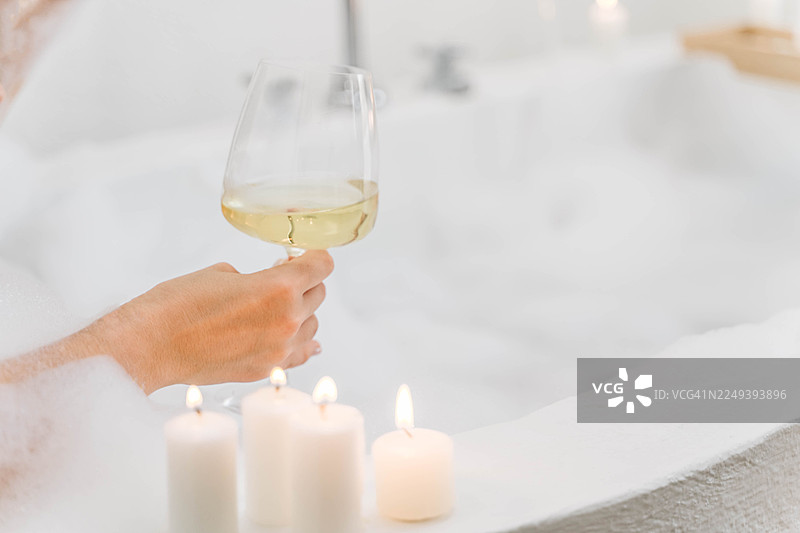 手持酒杯，前景有蜡烛。一位女士在泡澡，享受放松时刻。图片素材