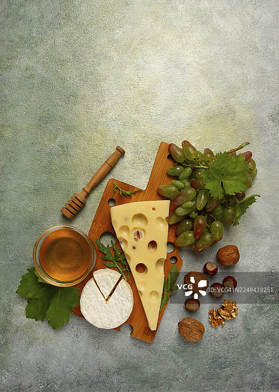 大孔奶酪，如艾门塔尔奶酪、马苏达奶酪、布里奶酪，放在砧板上，配有葡萄、蜂蜜和坚果，是佐酒的开胃菜，俯视图图片素材