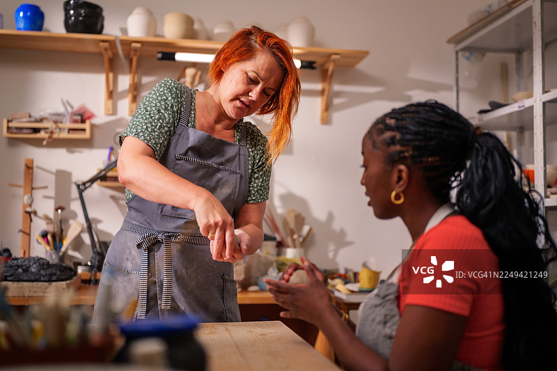 在一间陶艺工作室里，一位技艺娴熟的工匠在教导她的学徒如何精心准备陶土，以此分享她对陶瓷的热情，并激发创造力与连接感。图片素材