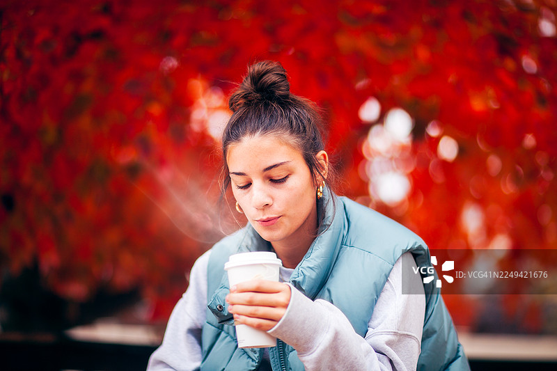 一位18岁的年轻女子在秋日户外享受热饮图片素材