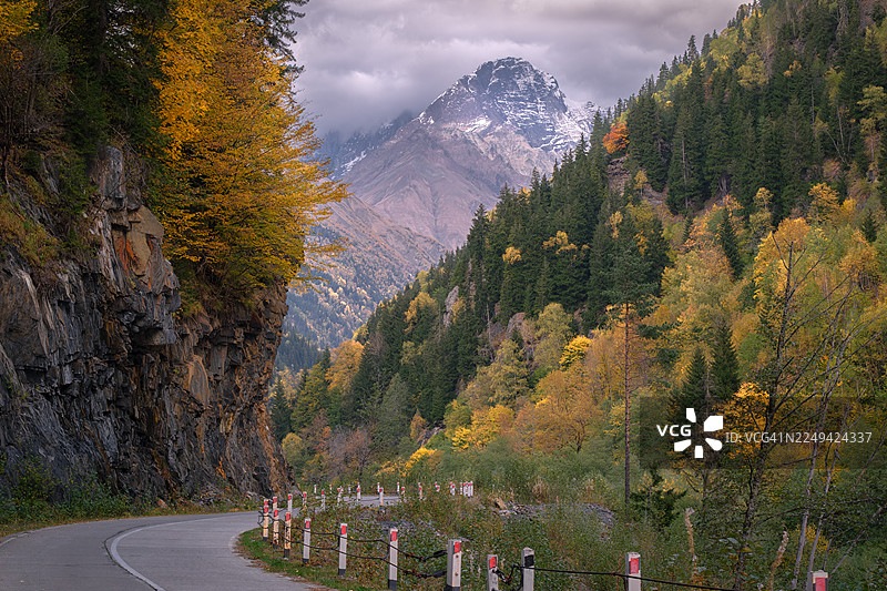 蜿蜒的山路穿过色彩鲜艳的秋季森林，远处是云层下的雪山之巅，佐治亚州图片素材