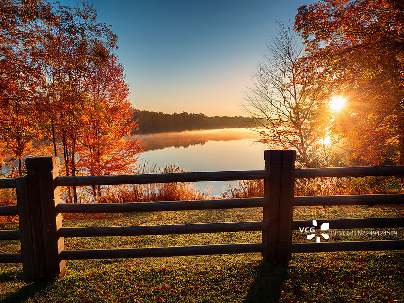 金色时分，基督城，新西兰。前景是质朴的木栅栏，背景是生机勃勃的秋季树木，宁静的湖面在金色余晖中闪耀，捕捉了大自然宁静之美。图片素材