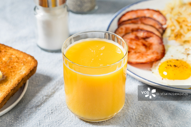美味丰盛的早餐，包括橙汁、吐司、鸡蛋和火腿，摆放在浅蓝色的桌布上图片素材