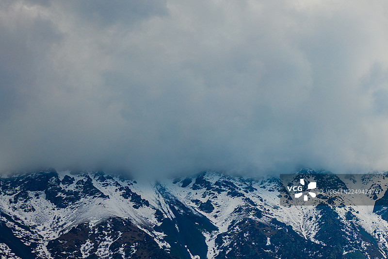 雄伟的雪山笼罩在戏剧性的云层中，营造出宁静而强大的自然景观图片素材