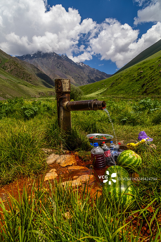 阳光明媚的日子里，潺潺的溪水从质朴的管道中流淌而出，流经郁郁葱葱的山谷，为西瓜和瓶子降温。图片素材