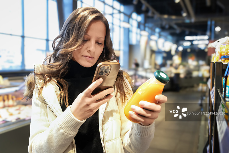 一名女子在现代超市过道里使用智能手机扫描商品图片素材
