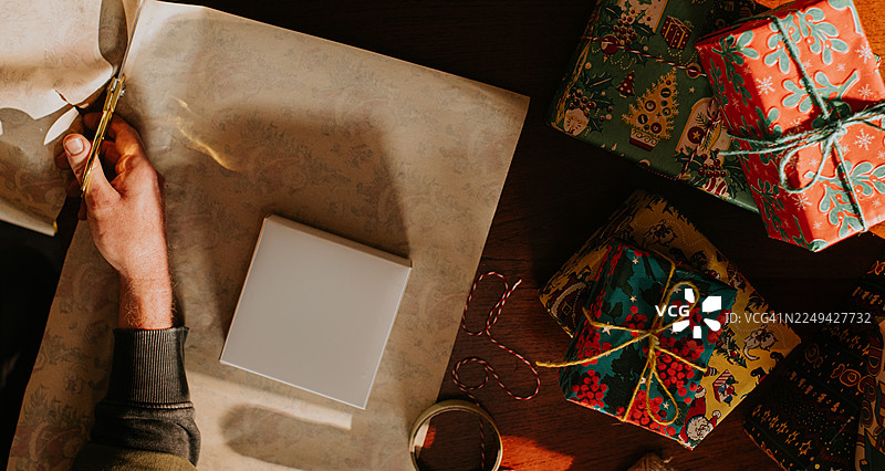 圣诞节礼品包装场景。一名男子正在裁剪他正在包装的小礼盒周围的包装纸。图片素材