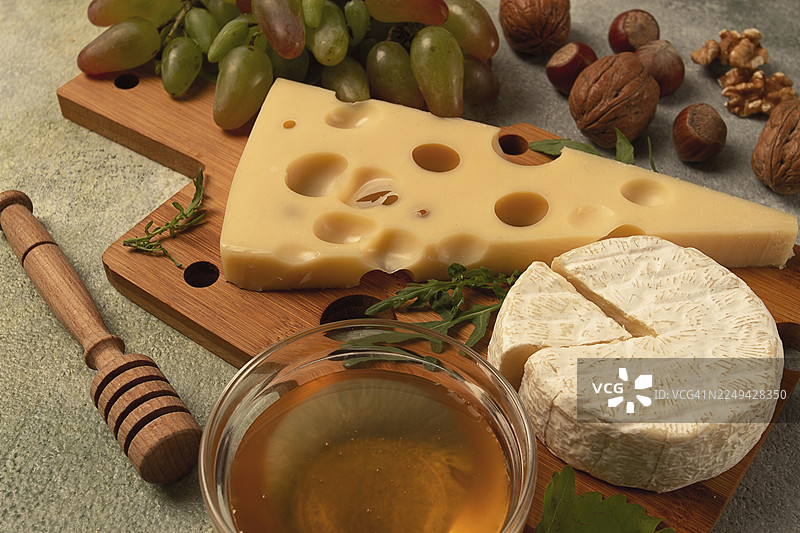 大孔奶酪，如艾门塔尔奶酪、马苏达奶酪、布里奶酪，摆放在砧板上，搭配葡萄、蜂蜜和坚果，是佐酒的开胃菜，俯视角度。图片素材