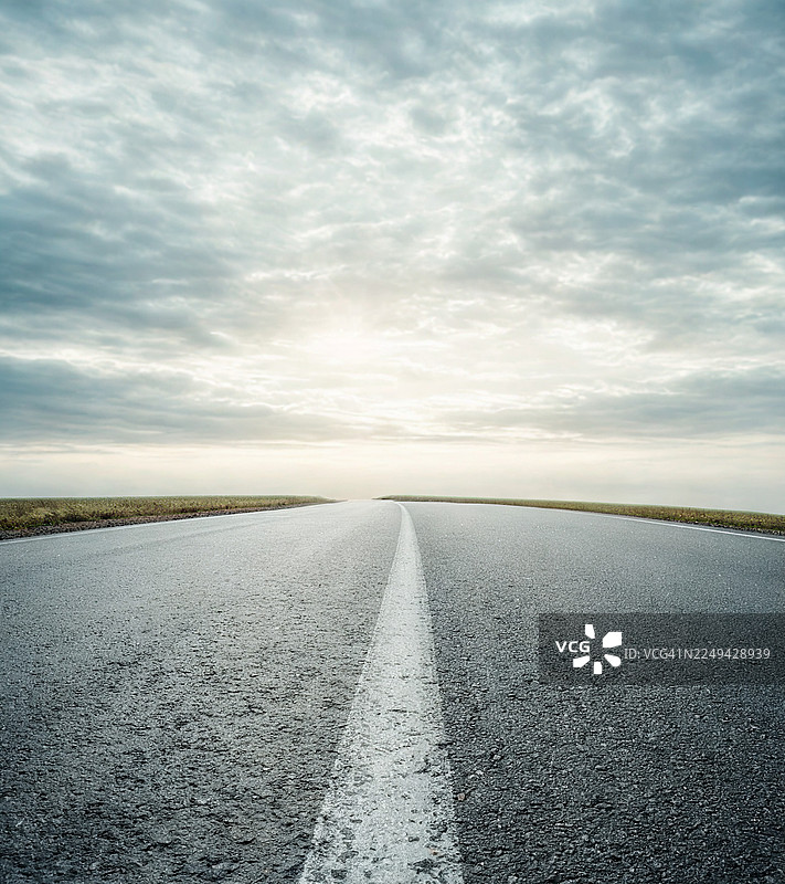 黎明或黄昏时，一条空旷的沥青路在戏剧性的多云天空下延伸至地平线。图片素材