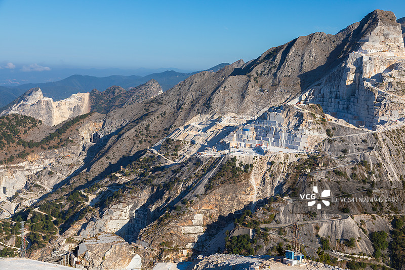 意大利亚平宁山脉中，在湛蓝天空下，一座大理石采石场被戏剧性地雕刻其中，呈现出壮观的空中视角。图片素材