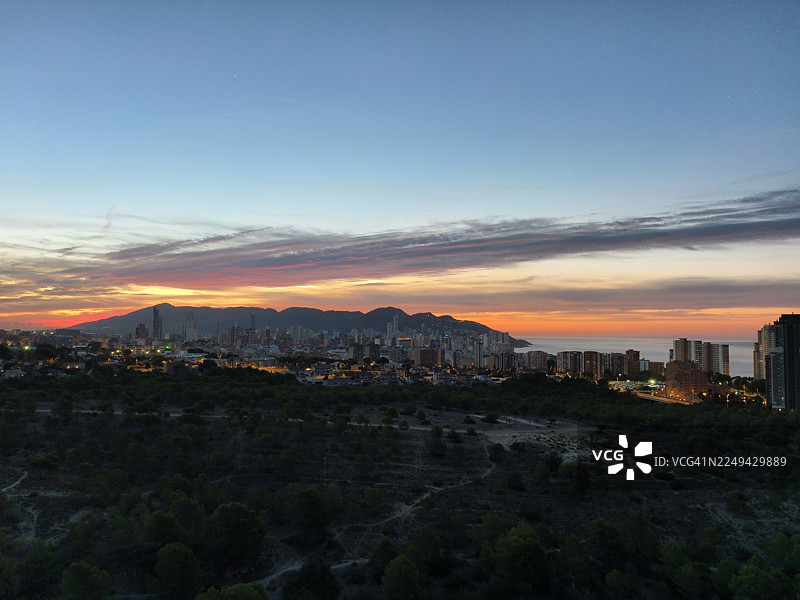夕阳下海滨城市的俯瞰视角，背景是群山，天空色彩斑斓，建筑灯火辉煌图片素材