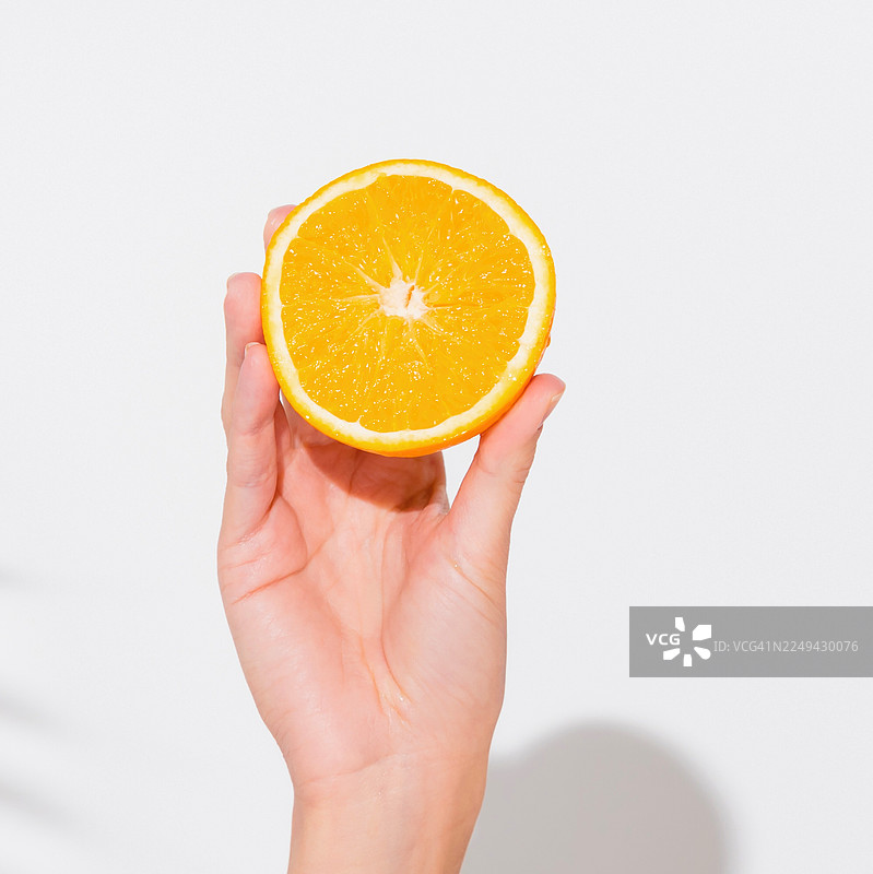 特写一只手握着鲜橙色的半个橙子，背景为干净的白色，展现出新鲜和健康饮食图片素材