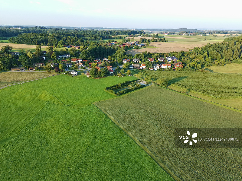 高空视角捕捉到一片由绿色农田和零散小村庄组成的拼布，在明亮的天空下，远方地平线依稀可见图片素材