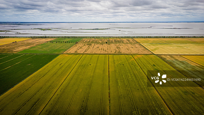 从空中俯瞰广阔的农田与大片水域在阴云密布的天空下交汇，意大利，科马基奥，波拉瓦莱佩加路图片素材