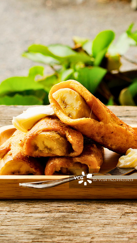 木质盘中金黄酥脆的炸香蕉卷配奶油，背景是乡村木桌和绿叶图片素材