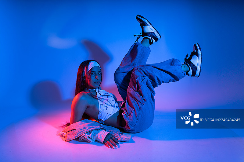 一位时尚年轻女子在蓝红霓虹灯下摆出戏剧性姿势，展现都市时尚。图片素材