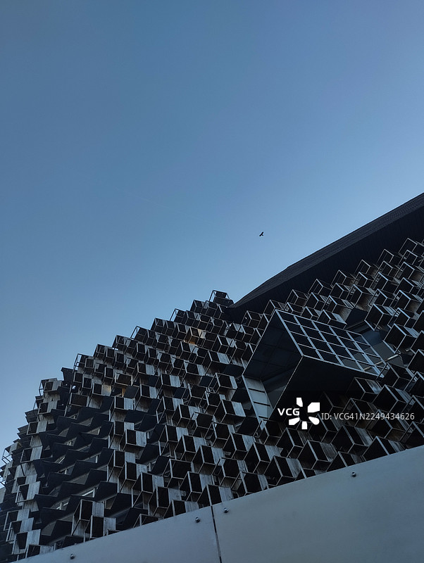 低角度仰视现代建筑，其纹理外观在晴朗的蓝天下，远处有一只飞鸟，印度尼西亚图片素材