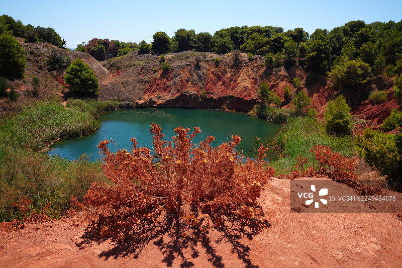 在湛蓝天空下，宁静的湖泊坐落在红土地山丘和葱郁植被之间，景色优美图片素材