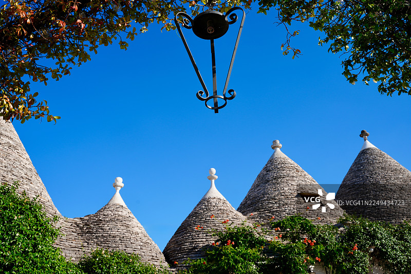 阿尔贝罗贝洛，意大利，传统特鲁利小屋，圆锥形石屋顶，在明媚的蓝天和绿色树叶的映衬下图片素材