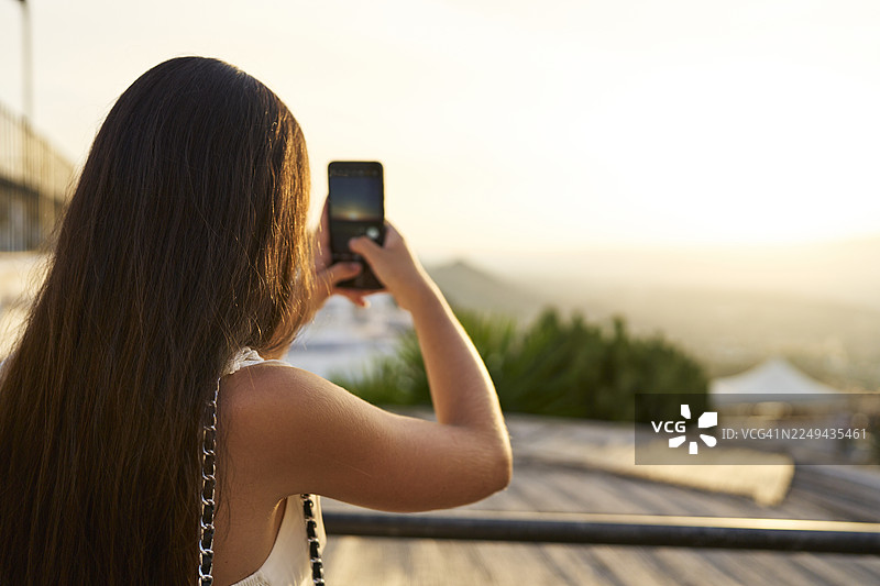 女子在度假时用智能手机拍摄日落图片素材