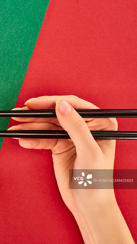 特写手持筷子，背景是鲜艳的红绿色图片素材