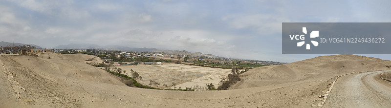 秘鲁帕查卡马克，阴天下的沙漠风光全景，远处的城镇，一条土路蜿蜒穿过干旱的地形图片素材