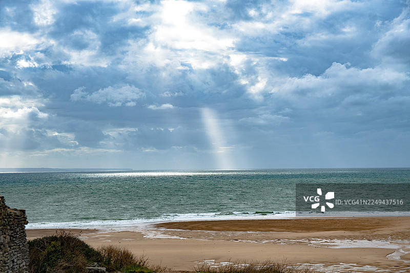 戏剧性的光线穿透多云的天空，掠过宁静的海洋和沙滩，构成一幅宁静而鼓舞人心的自然风光，法国图片素材