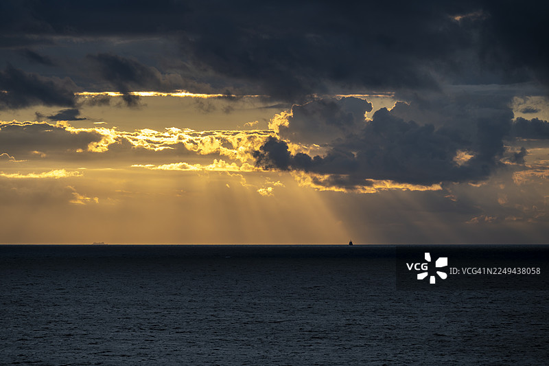 德国罗斯托克，戏剧性的日落景象，太阳光穿透乌云，照耀在海面上图片素材