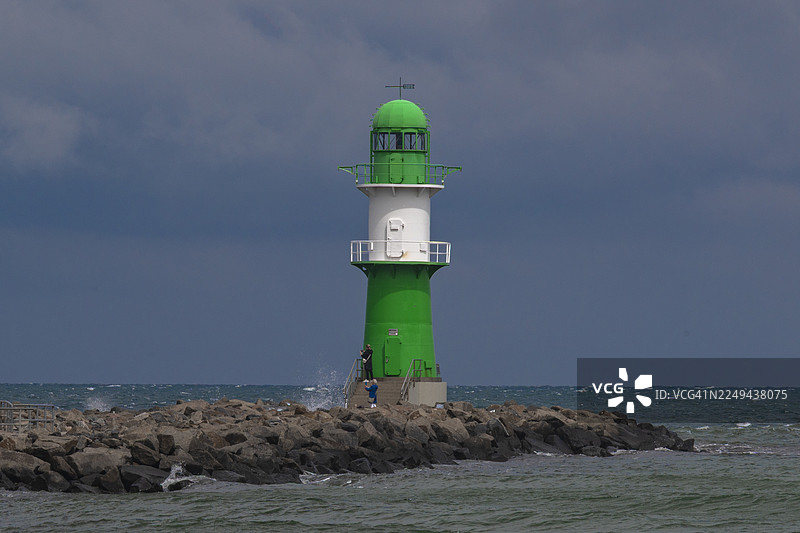 德国罗斯托克，岩石码头上的黑白灯塔，天空阴沉多云，海浪汹涌图片素材