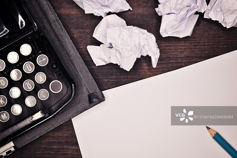 俯视角度拍摄的复古打字机、揉皱的纸张和铅笔放在木桌上，象征着写作和创作的挣扎图片素材