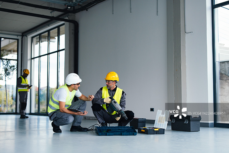 穿着高可见度背心和头盔的建筑工人正在新的办公空间里协作图片素材