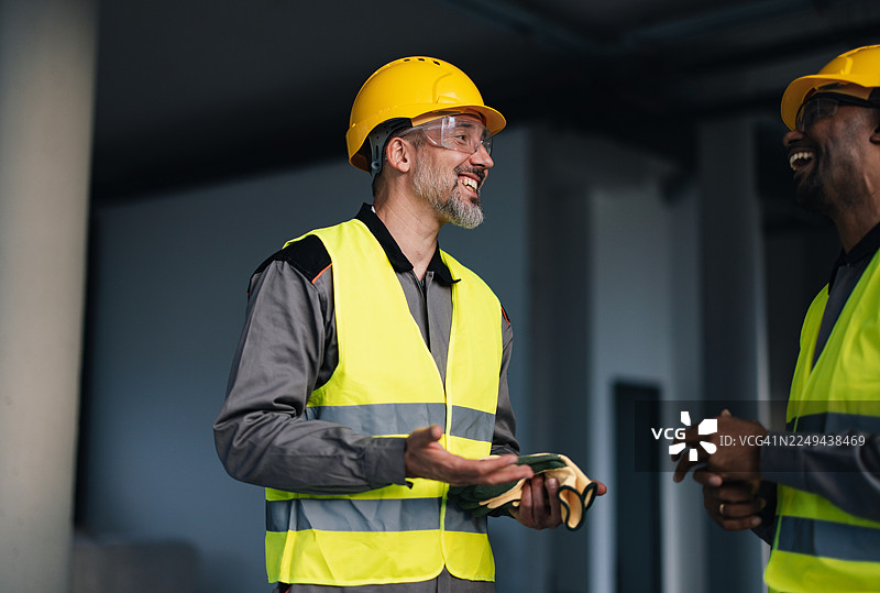 两位穿着高可见度背心和安全帽的建筑工人正在建筑工地上交谈图片素材