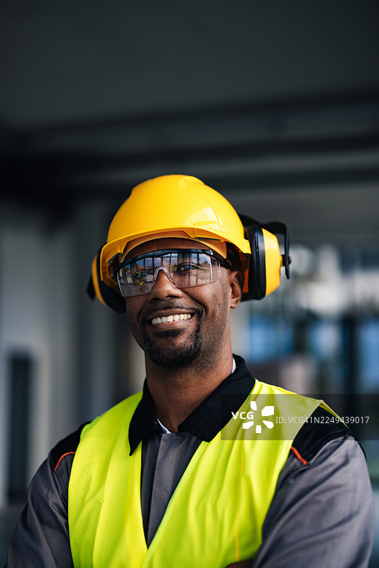 戴着黄色安全帽、穿着高能见度背心和安全装备的建筑工人正在工地上微笑图片素材