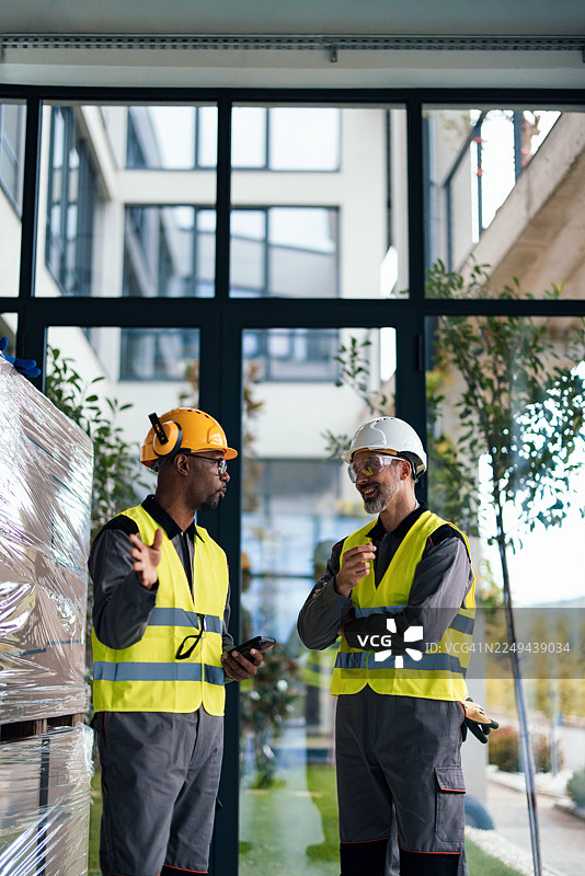 身穿高可见度背心的两位建筑工人正在现代办公楼建筑工地内讨论工作计划图片素材