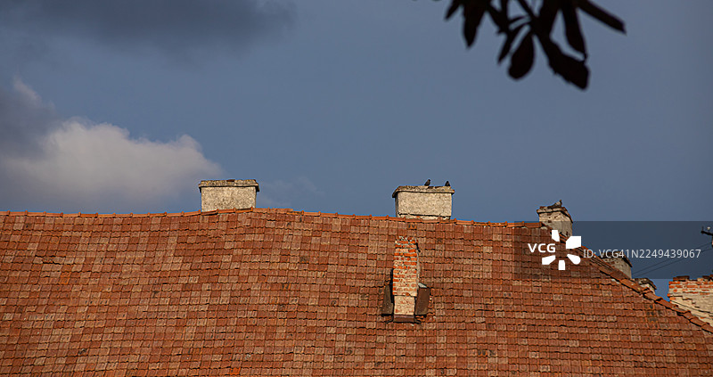 仰视角度拍摄的，布满烟囱的旧瓦屋顶在阴云密布的天空下图片素材