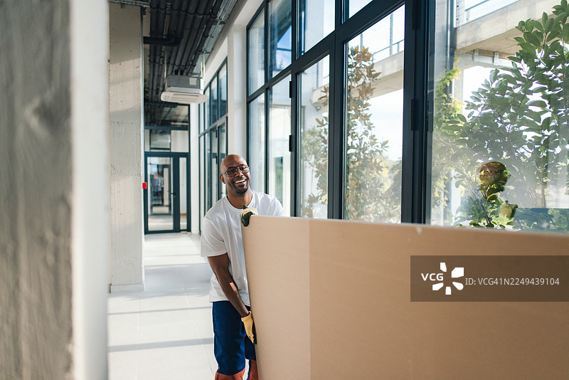 搬家过程中，快乐的工人在明亮现代的办公室走廊里移动大型隔断。图片素材