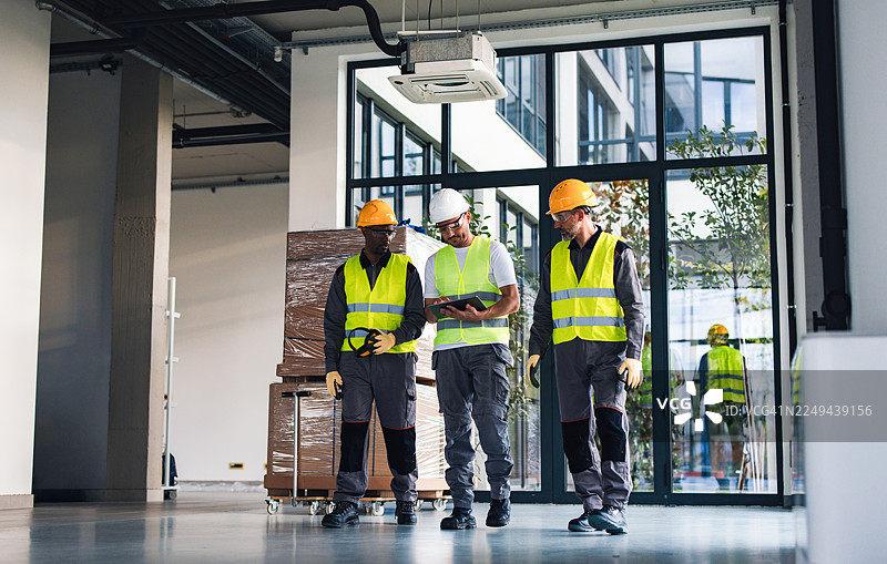 穿着安全装备的建筑工人在搬入新办公空间时在内部审阅计划图片素材