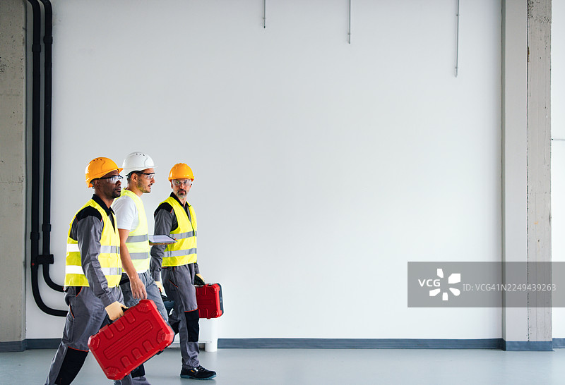 身穿安全背心的建筑工人团队在室内考察时携带工具箱图片素材