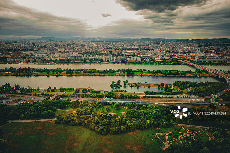 从高处俯瞰欧洲广阔的城市景观，有河流、桥梁和绿地，天空阴沉而富有戏剧性，位于奥地利维也纳。图片素材