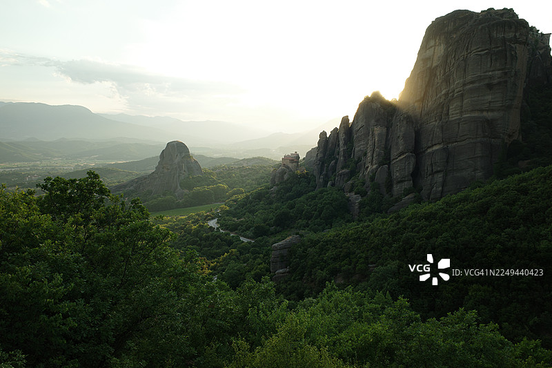 夕阳下，雄伟的岩石构造和郁郁葱葱的绿色山脉在明媚的天空下构成一幅宁静而开阔的风景画，希腊图片素材