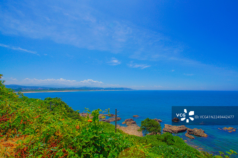 晴朗的一天，生机勃勃的蓝色天空映衬着广阔的海洋和葱郁的绿色海岸景观图片素材