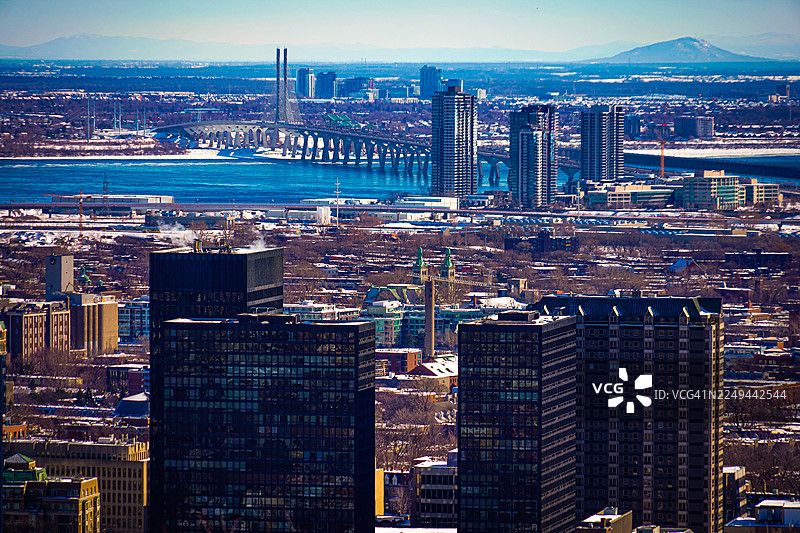 从空中俯瞰城市，有河流和桥梁，周围是白雪覆盖的风景，天空晴朗，加拿大图片素材
