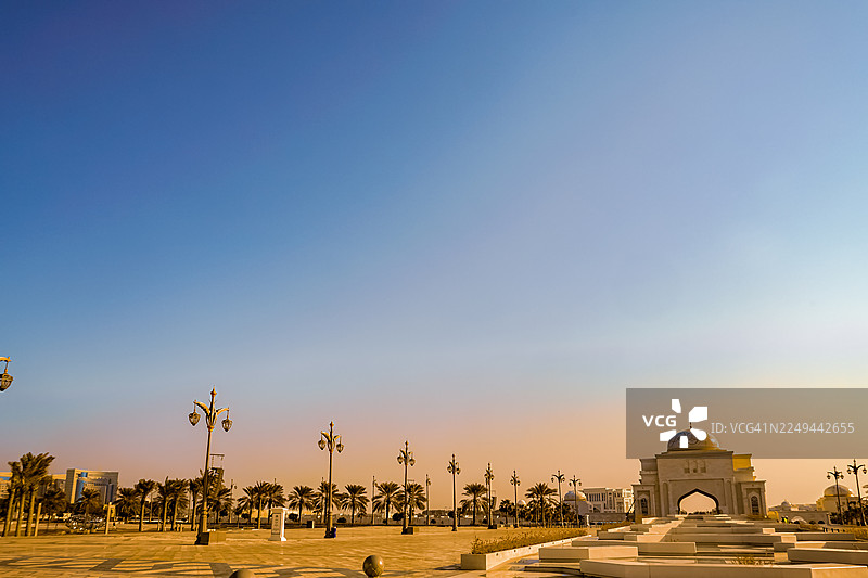 日落时分，晴朗的蓝天下，阿布扎比，阿拉伯联合酋长国，棕榈树和华丽的建筑映衬着宏伟的城市景观图片素材